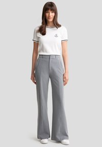 T-shirt blanc avec des bords noirs, logo sur la poitrine, associé à un pantalon ample gris taille haute. Tenue complétée par des baskets blanches.