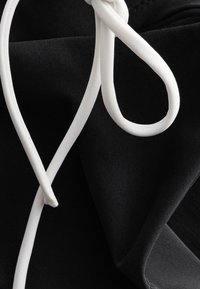 Cordon blanc noué en un nœud lâche sur un tissu noir, probablement un sweat à capuche ou un pantalon de jogging, montrant la texture et les plis du matériau.