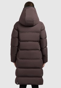 Brun pufferjakke med hætte, med quiltet design, lange ærmer og længde til midt på læggen. Glat tekstur, minimal hardware accenter.