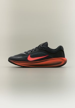 Czarno-czerwony but do biegania Nike z dużym czerwonym logo, cholewką z siateczki i amortyzowaną podeszwą na jednolitym neutralnym tle.