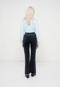 Zilā garenās piedurknēs kreklu un tumšas ūsras bikses, kas izgatavotas no mīkstas auduma. Biksēm ir augsts josta un smalks raksts, ko papildina melni apavi.