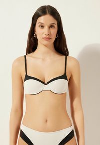 Vit texturerad bikiniöverdel med svarta accenter, med underwirestöd, tunna justerbara strängar och en sömlös design.