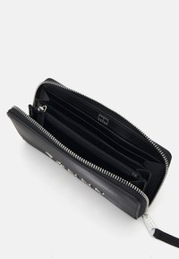 Černá kožená peněženka se stříbrným zipem a kováním. Obsahuje více přihrádek na karty, zipovou kapsu, hladký povrch a organizovaný interiér.