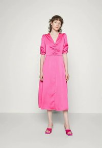 Vestido de cetim rosa com mangas bufantes, decote em V e detalhe franzido no corpete. Comprimento até a metade da panturrilha, combinado com sandálias rosa de slide a condizer.