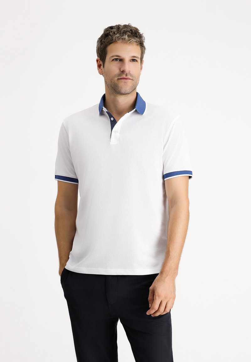 Camisa polo blanca con acentos azules en el cuello y las mangas. Presenta un diseño clásico con una tapeta de dos botones y tela texturizada.