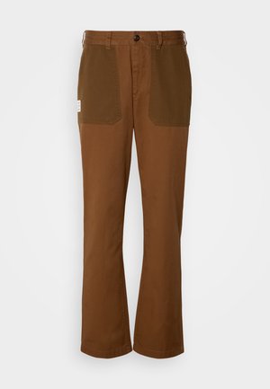 Barna nadrág egyenesen szabott fazonban, az elülső zsebeknél kontrasztos sötétebb barna panelek találhatók, és egy gombbal záródik.