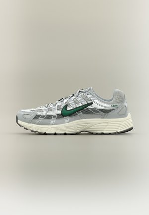 Baskets Nike P-6000 grises et blanches avec logo swoosh vert et semelle texturée, vues de profil sur un fond beige uni.