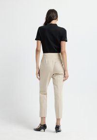Zwarte korte mouwen top, beige high-waisted broeken met voorplooien en zwarte gesloten schoenen. Eenvoudig ontwerp, tailored fit.