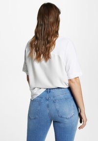 Camiseta blanca de corte relajado con mangas cortas, combinada con jeans de denim azul de tiro medio. La camiseta presenta una textura suave y un diseño casual.