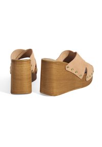 Tansuede wedge-heeled klompen met een uitsnijdingen. Kenmerkt zich door goudkleurige studs langs de randen en een getextureerde houten hak.
