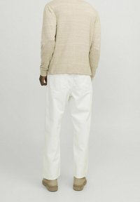 Beżowa koszula z długim rękawem o subtelnej fakturze, zestawiona z luźnymi białymi spodniami i beżowymi butami, widoczna z tyłu.