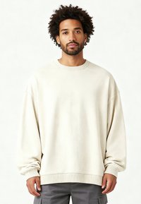 Felpa oversize off-white con collo rotondo, maniche lunghe, polsini a coste e una texture liscia. Caratterizzata da una vestibilità rilassata e un design minimalista.