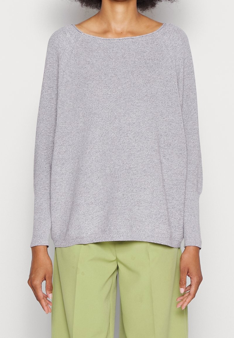 Maglione grigio lavorato a maglia con scollatura ampia, spalle cadenti e maniche lunghe, abbinato a pantaloni verde chiaro; il tessuto ha un aspetto strutturato.