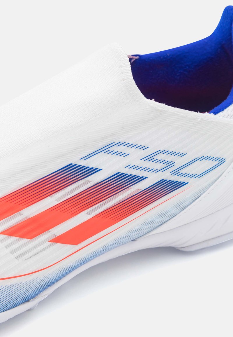 Zapatilla atlética blanca con textura suave, con acentos en azul y rojo, forma aerodinámica y un cuello ajustado para facilitar su uso.
