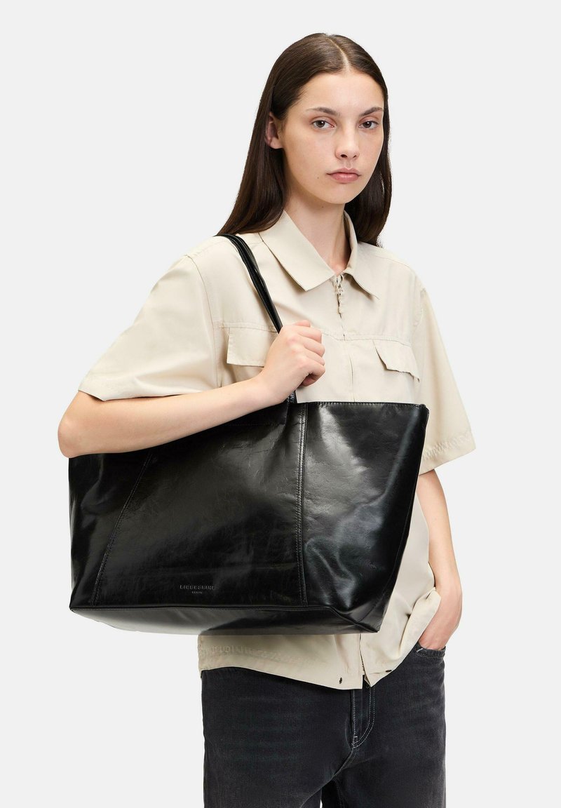 Czarna skórzana torba tote o gładkiej teksturze, prostokątnym kształcie, długich uchwytach i minimalistycznym designie. Posiada subtelne detale w postaci przeszyć.