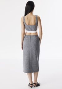 Top corto a maglia grigia con una larga fascia bianca sotto il busto; abbinato a una gonna grigia fino al ginocchio con zip posteriore e dettagli delle cuciture.