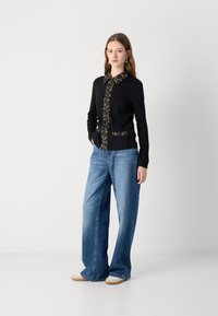 Zwarte cardigan met een gekleed kraag en zakken, gecombineerd met wijde blauwe jeans en lichte sneakers. Soepele textuur en een ontspannen pasvorm.