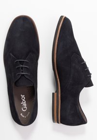 Tmavě modré oxfordské boty z broušené kůže, vyznačující se hladkým nártem, kulatou špičkou a plochou hnědou gumovou podrážkou s minimalistickým šněrováním.