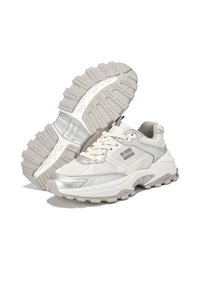 Zapatillas blancas con una parte superior de malla y detalles en plateado, suela de goma gruesa con un dibujo texturizado, y áreas de puntera y talón reforzadas.