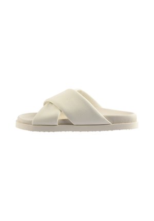 Kremowy klapek na płaskiej podeszwie z szerokimi, wyściełanymi skrzyżowanymi paskami, widoczny z boku na białym tle.