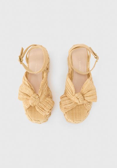 Woven espadrille sandals in light beige with a knotted bow design, an ankle strap, and a textured, braided sole.