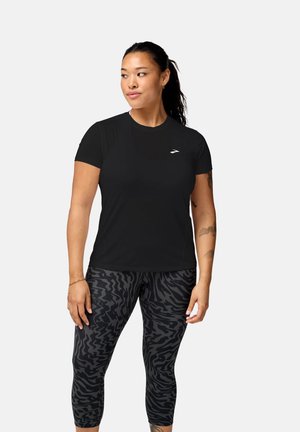 Maglietta sportiva nera a maniche corte con un logo sottile, abbinata a leggings neri a vita alta con un motivo a strisce zebrate scure.