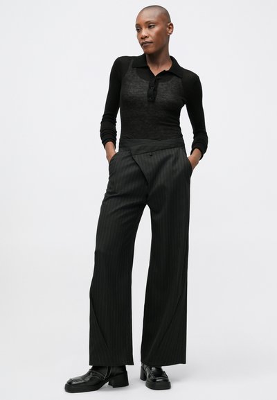 Crna, priljubljena majica dugih rukava s ovratnikom i detaljem gumba, uparena s širokim crnim hlačama na pruge i mokasinkama.