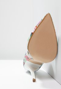 Chaussure à talon haut à motif floral avec un bout pointu, en matériau brillant, et une semelle beige avec une texture striée.
