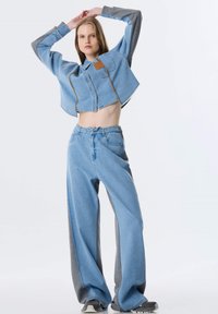Afgekorte spijkerjas met grijze mouwen, blauwe wijde jeans met grijze zijpanelen. Beide hebben een casual, comfortabele pasvorm en zichtbare stiksels.