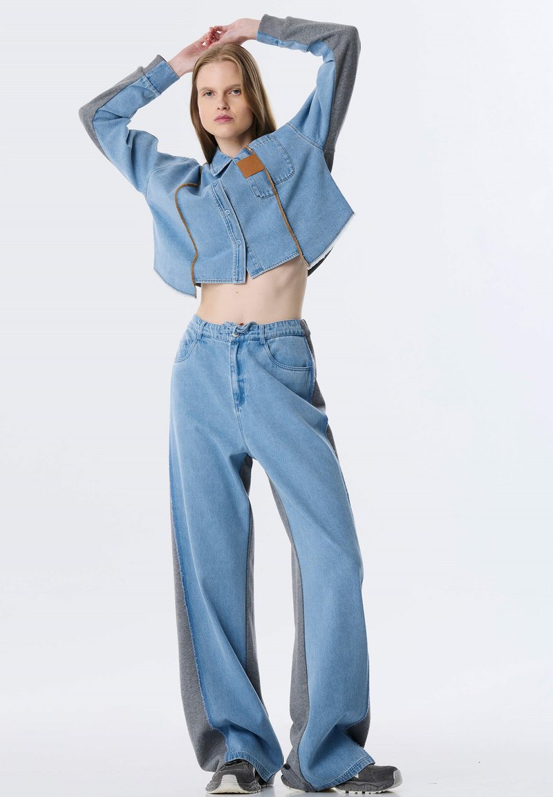 Afgekorte spijkerjas met grijze mouwen, blauwe wijde jeans met grijze zijpanelen. Beide hebben een casual, comfortabele pasvorm en zichtbare stiksels.