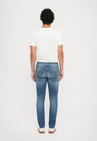 Μπλε τζιν παντελόνι με ξεθωριασμένο εφέ, που διαθέτει πέντε τσέπες, ραφές και σχεδίαση slim fit. Φοριέται με λευκή μπλούζα.