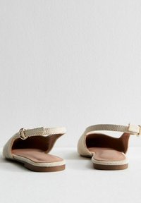 Beige vävda sandaler med öppen bak, platt sula och en guldbuckle som accent. Slät innersula ger komfort och stöd.