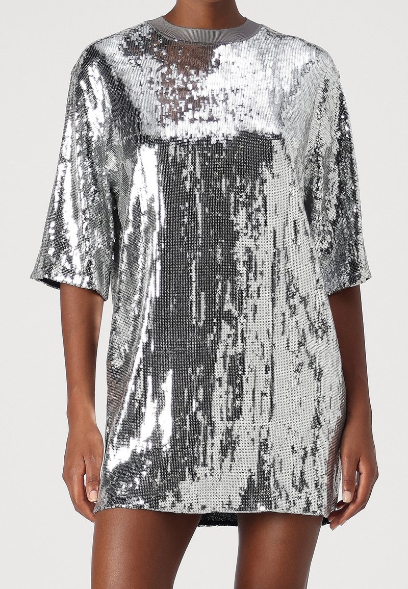 Robe mini à manches courtes en sequins argentés brillants portée par une personne à la peau foncée, coupée au niveau du cou et du milieu de la cuisse, debout sur un fond uni.