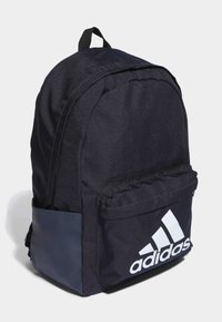 Zaino in tessuto nero con una forma strutturata, dotato di un ampio scomparto principale, tasca frontale e logo Adidas bianco sul lato.