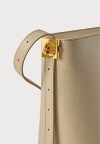 Beige lederen handtas met een gladde textuur, voorzien van een vierkante gouden sluiting en een verstelbare riem met meerdere gaatjes.