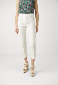 Pantalones blancos ajustados y recortados con corte a medida y parte delantera plana. Combinados con sandalias de tacón alto beige con un acento de hebilla.