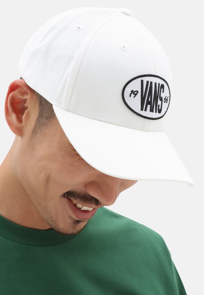 Gorra de béisbol blanca de algodón con visera redondeada, que presenta un parche ovalado negro con el texto "VANS 66" en el centro.