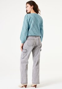 Gestructureerde lichtblauwe cropped trui met lange mouwen, gecombineerd met grijze hoogwaist cargo broeken en beige schoenen met een driehoekige hak.