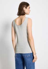 Top grigio senza maniche con scollatura rotonda sul retro, realizzato in tessuto morbido, abbinato a jeans larghi blu. Design semplice e aderente.