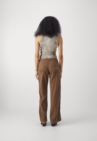 Bruna byxdresser med vida ben och strukturerad yta, med bakfickor, kombinerade med en åtsittande, ljusgrå tanktopp med en diskret mönstring.