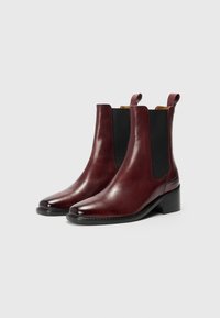 Burgunderfargede lær Chelsea-boots med svarte elastiske sidelapper, spiss tå og lav blokkhæl. Har påtrekksløkker for enkel bruk.