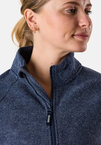 Giacca blu navy con zip, colletto alto, tessuto texturizzato e dettagli della zip a contrasto. Presenta un motivo a righe discreto.