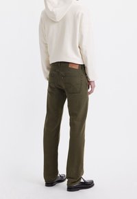 Kalhoty z kordurové látky olivově zelené barvy se rovnými nohavicemi a viditelnými zadními kapsami, doplněné krémovou mikinou s kapucí a černými mokasíny.