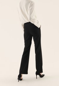 Černé kalhoty se přímým střihem, vyrobené z měkké látky, v kombinaci s bílou blůzou a černými lodičkami. Viděno zezadu.