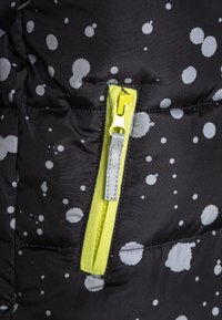 Černá zimní bunda s kašmírovým vzorem v šedé barvě. Obsahuje žlutý zip a šedou šňůrku na zip, s prošívanou strukturou.