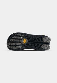 Semelle de chaussure en caoutchouc noir avec de profonds crampons et un motif texturé, comportant un logo jaune bien visible près de la zone du talon pour améliorer la traction.