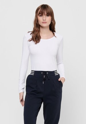 Long-sleeve white top with a round neckline, paired with black drawstring pants featuring white striped accents at the waist.