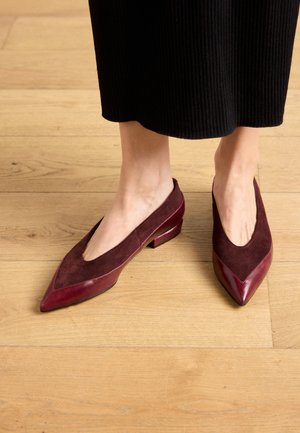 Ballerine bordeaux con punta appuntita, in suede e dettagli in pelle lucida, dotate di un piccolo tacco a blocco per stabilità.