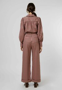 Completo due pezzi a scacchi rosa e nero con colletto arricciato e pantaloni a gamba larga, caratterizzato da maniche lunghe e tasche posteriori.