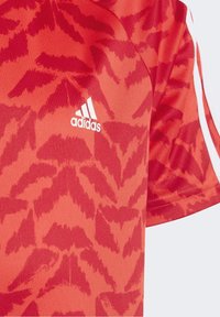 Röd sporttröja med bladliknande mönster, av slät tyg, med vit Adidas-logotyp på vänster bröst och kontrasterande sidostripes.
